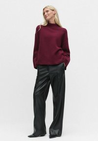 Bourgogne stickad tröja med hög krage, i kombination med svarta byxor i konstläder med vida ben. Slät textur och avslappnad passform.