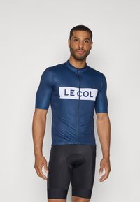 Maillot de cyclisme bleu marine à manches courtes, avec une fermeture éclair à l'avant et un emblème blanc portant la mention "LE COL". Assorti à un short de cyclisme noir.