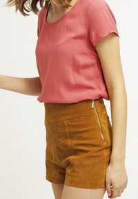 Pink short-sleeve top with a round neckline paired with brown, high-waisted suede shorts featuring a side zipper detail.