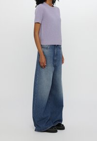 Maglione corto a maniche corte di colore viola chiaro, abbinato a jeans in denim blu sbiaditi e oversize, e scarpe nere con suola spessa.