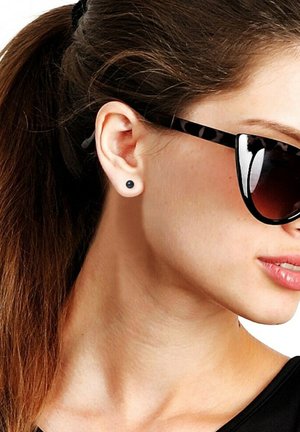 Des lunettes de soleil noires avec des taches, équipées de verres sombres, portées avec une petite boucle d'oreille noire. Les cheveux sont attachés en arrière, dévoilant l'oreille et le cou.