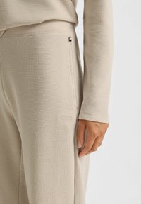 Beige waffle-knit broek met zijzak en bijpassend lang mouwtop, hand ontspannen aan de zijkant, geborduurd BOSS-logo nabij de zak.