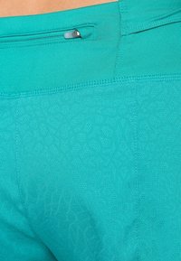 Leggings de rendimiento en turquesa que presentan un patrón texturizado, una cinturilla ancha y un bolsillo con cremallera discreto en la parte trasera.