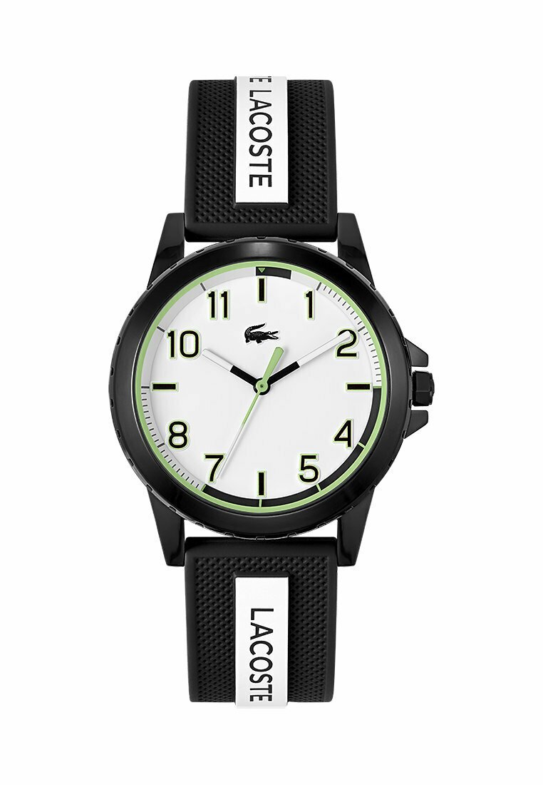 Montre noire avec un grand cadran blanc, des accents verts et de grands chiffres noirs. Elle présente un bracelet en caoutchouc noir texturé avec un logo Lacoste.