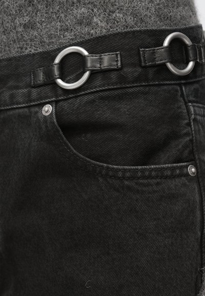 Fekete farmernadrág ezüst gyűrűvel, amely bőrszíjhoz van rögzítve a derékpántnál, elöl zsebbel és látható varrási részletekkel.