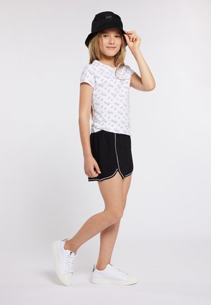 Witte T-shirt met een subtiel grijs patroon, zwarte shorts met witte accenten, en witte sneakers. Een zwarte bucket hat maakt de outfit compleet.