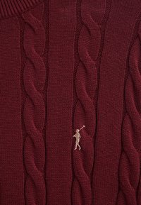 Maglione bordeaux a trecce realizzato in filato morbido, con motivo testurizzato e piccolo logo a contrasto ricamato sul davanti.