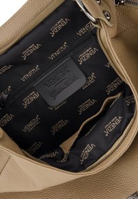 Intérieur d'un sac à main en cuir beige texturé avec doublure en tissu noir. Dispose d'une poche zippée et d'un logo "VENEZA" en relief sur le panneau.