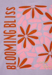 Lavendli kangas oranžide tikanditega lillede ja sõnaga "BLOOMING BLISS" oranžis ning osaliselt kurrulise kirjaga helekollases.