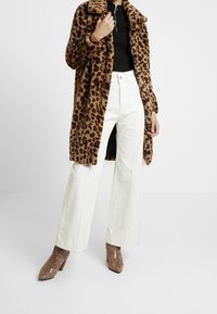 Cappotto in faux fur con stampa leopardata, pantaloni bianchi a gamba larga e stivali marroni con motivo a serpente. Tessuto testurizzato e dettagli del colletto ben definiti.