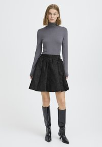 Gray turtleneck sweater paired with a black floral-patterned skirt. Model wears knee-high black glossy boots. Simple, fitted silhouette.