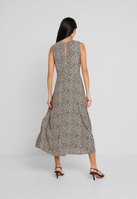 Hihaton, polviin saakka ulottuva mekko vaaleasta kankaasta, jossa on mustia pisteitä, avaimenreikä takaosassa ja virtaava hame.