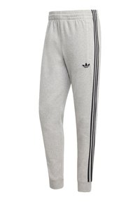 Sivé tepláky s čiernym logom Adidas, ktoré majú čierne bočné pruhy, elastický pás a manžety na členkoch.