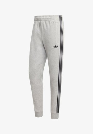 Sivé tepláky s čiernym logom Adidas, ktoré majú čierne bočné pruhy, elastický pás a manžety na členkoch.