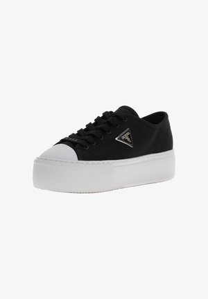 Baskets basses noires avec semelle plateforme blanche, protection blanche au niveau des orteils, lacets noirs et logo métallique triangulaire Guess sur le côté.