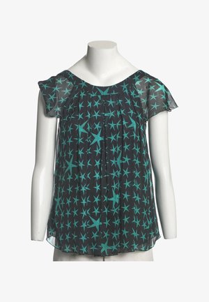 Blouse noire transparente avec manches courtes volantées et motif d'étoiles turquoise sur un buste de mannequin blanc.