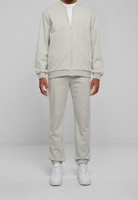 Ljusgrå zip-up sweatshirt och matchande joggers av mjukt material, med ribbade manschetter och en ren design. Bärs med vita sneakers.