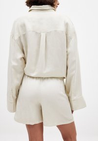 Lichtbeige linnenoutfit bestaande uit een langemmouwen blouse en bijpassende shorts met een elastische tailleband. Zachte textuur en een relaxte pasvorm.