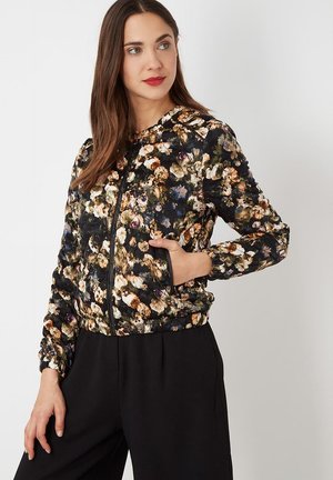 Chaqueta bomber floral en negro con estampado floral multicolor, que presenta un cierre de cremallera en la parte delantera, capucha y puños elásticos con bolsillos laterales.