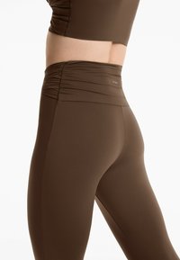 Bruna högmidjade leggings med en texturerad, rynkad midjeband. Tillverkade av ett smidigt och elastiskt tyg. Logodetalj nära midjebandet.