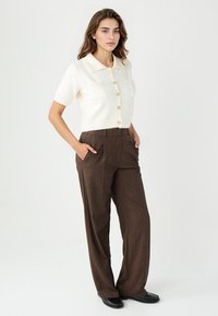 Korte mouw ivoren cardigan met een kraag en knopen, gecombineerd met bruine hoog-getailleerde gestreepte broek en zwarte schoenen.