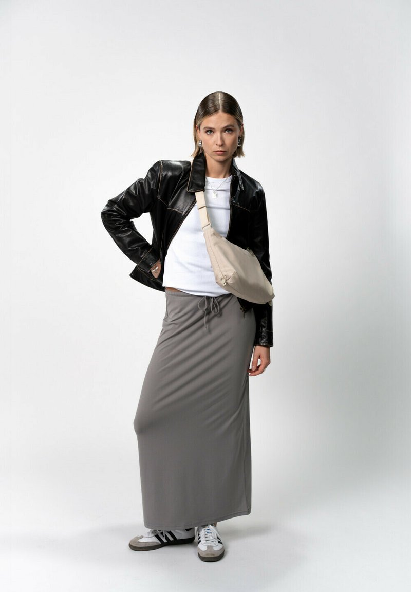 Giacca di pelle nera, t-shirt bianca, gonna lunga grigia, borsa a tracolla beige e sneakers bianco e nere; texture morbide e design casual.