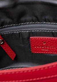 Interieur van een rode leren tas met een zwarte stoffen voering, voorzien van een ritszak en een goudgegraveerd rood label met de tekst "LAZAROTTI."