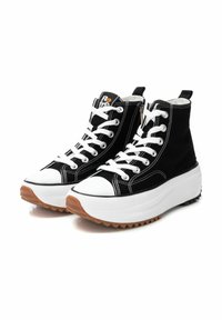Zapatillas de deporte altas negras con cordones blancos, tela negra texturizada, punta de goma blanca, suela intermedia blanca gruesa y suela exterior de goma marrón.