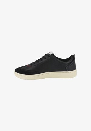 Baskets noires en cuir avec un embout texturé noir, une semelle en caoutchouc blanche et un détail de couture rouge sur la tige.