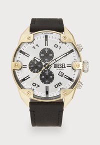 Reloj de tono dorado con esfera blanca, subesferas negras, correa de cuero negra gruesa y marcadores de horas prominentes. Cuenta con funciones de cronógrafo.