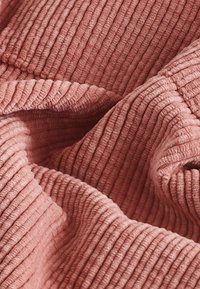 Stof in stofroze met een ribbelstructuur, met zachte, geplooide plooien. Het materiaal lijkt pluche en gezellig, geschikt voor dekens of zachte meubelbekleding.