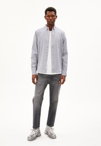 Lichtblauwe overhemden met een witte T-shirt, grijze jeans en grijze sneakers. Het shirt heeft een kraag en knopen aan de voorkant.