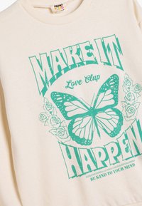 Sudadera crema con estampado gráfico en turquesa de una mariposa y rosas, con el texto "HAZ QUE SUCEDA" y "Love Club."