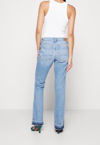 Pantalones vaqueros de denim azul claro, acampanados y de tiro medio, con dobladillo deshilachado y dos bolsillos traseros. Combinados con una camiseta sin mangas blanca y tacones en color verde azulado.