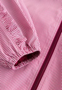 Tissu rayé rose et blanc avec des détails de poignets élastiques et une fermeture éclair bordeaux. Texture lisse avec une doublure intérieure douce.