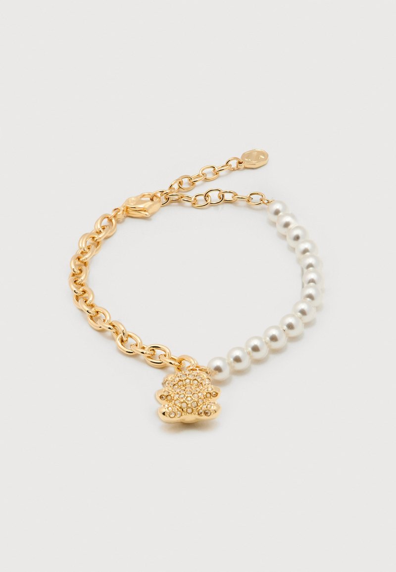 Gouden ketting en witte parelarmband met een gouden teddybeerbedel versierd met kleine kristallen op een witte achtergrond.