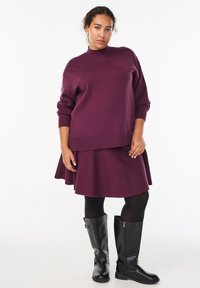 Violetti neulepusero, jossa on pyöreä kaula-aukko, yhdistettynä samanlaiseen hameeseen. Mustat polvipituiset saappaat vetoketju-yksityiskohdalla. Sujuva pinta.