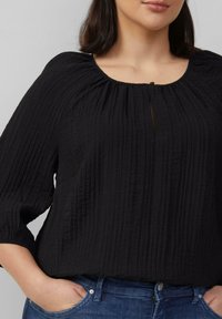 Zwarte, gekreuke textielblouse met een ronde hals en een kleine keyhole-details aan de voorkant. Lange, iets opgeblazen mouwen. Casual pasvorm.
