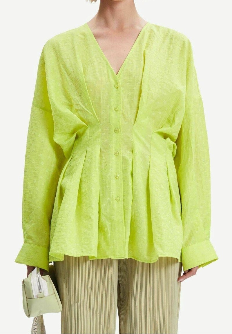 Camicia leggera a maniche lunghe di colore verde lime, con scollo a V, abbottonatura frontale e dettagli arricciati in vita. Tessuto texturizzato.