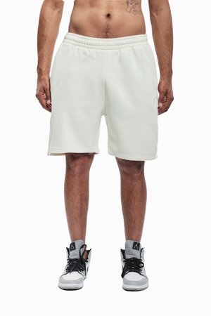 Pantalones cortos de mezcla de algodón color crema con cintura elástica, bolsillos laterales y corte relajado, combinados con zapatillas altas en gris y blanco.