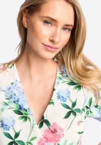 Bloemige wikkeljurk met blauwe en roze bloemen op een lichte stof. V-halsontwerp met bladranden, die een zachte textuur en levendige kleuren toont.