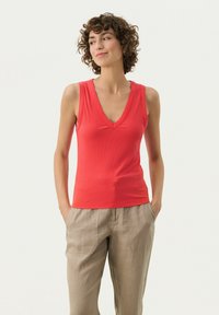 Rød ribbet tanktop med dyb V-hals-design, parret med beige linned bukser med forlommer. Glat tekstur, tætsiddende stil.