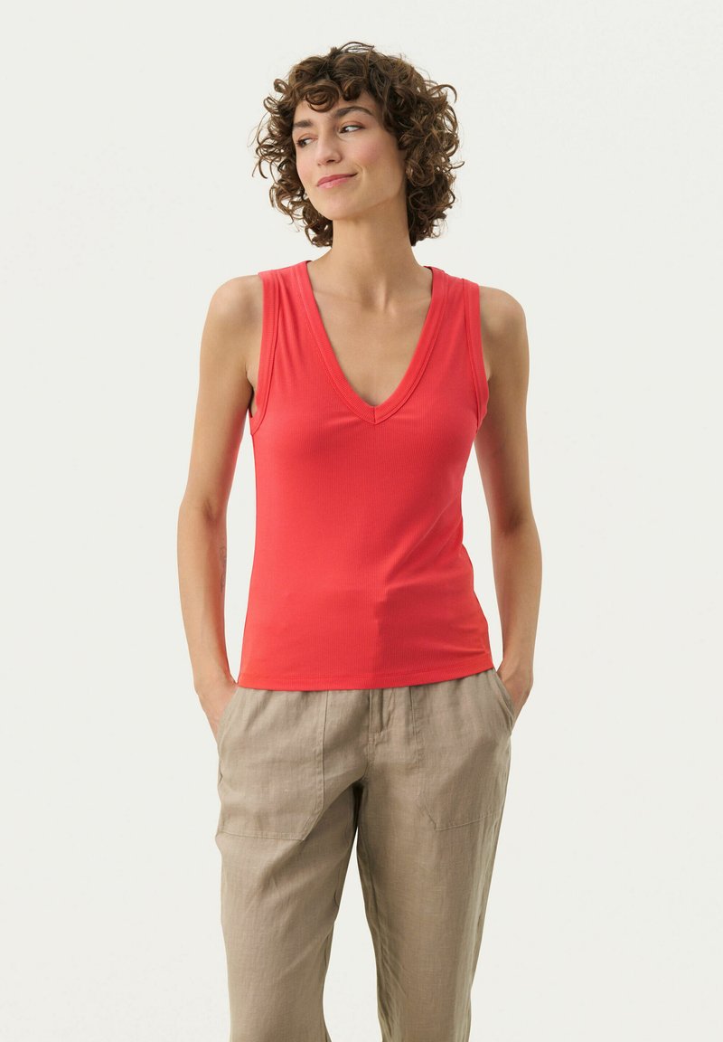 Rød ribbet tanktop med dyb V-hals-design, parret med beige linned bukser med forlommer. Glat tekstur, tætsiddende stil.
