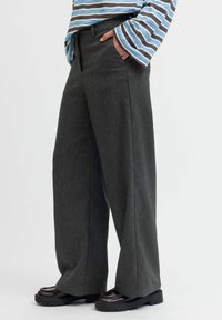 Pantalons à jambes larges en tissu texturé gris foncé, avec une taille haute et des plis avant, associés à des chaussures noires chunky.