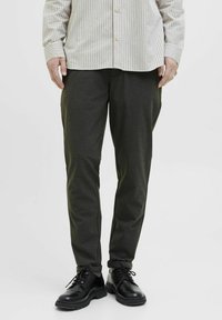 Pantaloni verzi închise, cu o croială ajustată, realizați dintr-un material neted. Asortați cu pantofi negri cu șiret, având o talpă texturată.