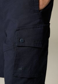 Pantaloni scurți cargo bleumarin dintr-un material texturat, cu un buzunar lateral, dotati cu închidere tip buton și brand embosat aproape de tiv.