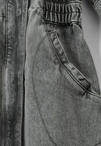 Grå denimjacka med en insydd midja, stora sidofickor och subtil textur med diagonala sömnadsinslag.