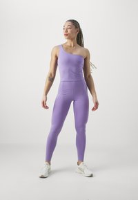 Levendula egyvállas body, amely feszes fazonú, összeillő leggingssel párosítva. Az anyag sima, elasztikus és testhez álló. Fehér tornacipők.