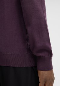 Maglione viola lavorato a maglia con polsini e orlo a coste, caratterizzato da un motivo testurizzato sui lati. Tessuto morbido e leggero, design aderente.