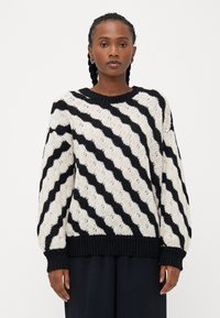 Maglione a maglia grossa in bianco e nero con righe a zig zag, scollatura rotonda e polsini e orlo a coste. Texture morbida, vestibilità oversize.